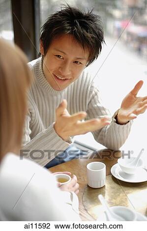 Stock Image - Young couple at a restaurant, talking, man with hands raised. Fotosearch