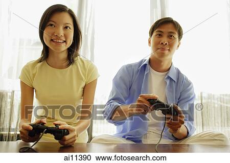 Stock Image - Young couple side by side, playing with handheld video game. Fotosearch