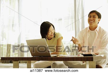 Stock Photo - Young couple sitting in front of laptop, talking. Fotosearch
