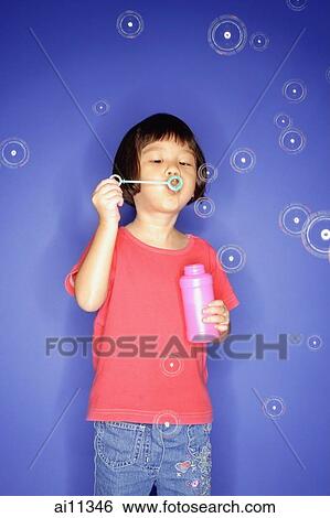 Stock Photograph - Young girl blowing bubbles, blue background. Fotosearch