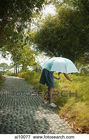 Young girl holding an umbrella, bending to look at something View Large Photo Image Stock Photo - Young girl holding an umbrella, bending to look at something. Fotosearch