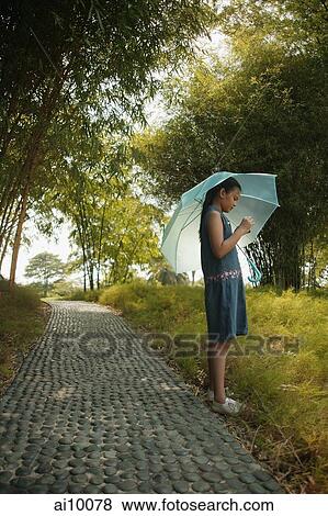 Stock Photo - Young girl holding an umbrella, looking at something. Fotosearch