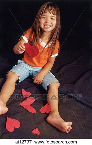Stock Photo - Young girl holding paper hearts, looking at camera. Fotosearch