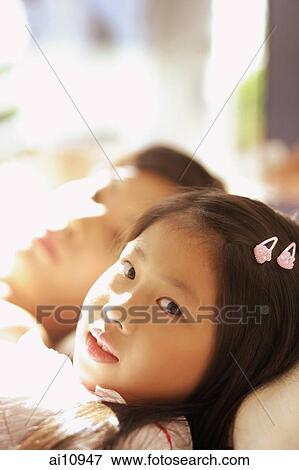Young girl lying next to her mother, looking at camera View Large Photo Image Stock Photo - Young girl lying next to her mother, looking at camera. Fotosearch