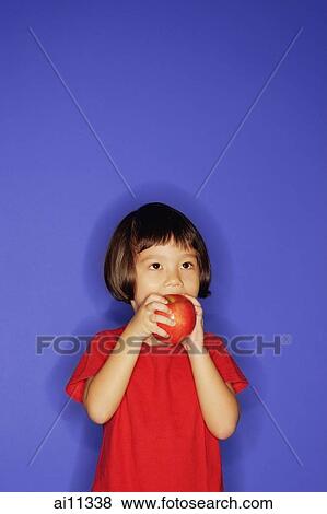 Young girl standing against blue background, eating an apple View Large Photo Image Stock Photo - Young girl standing against blue background, eating an apple. Fotosearch