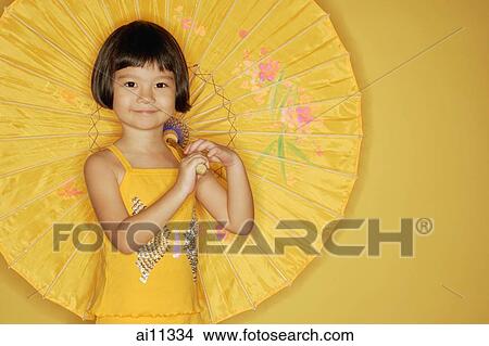 Young girl standing against yellow background, holding umbrella View Large Photo Image Picture - Young girl standing against yellow background, holding umbrella. Fotosearch