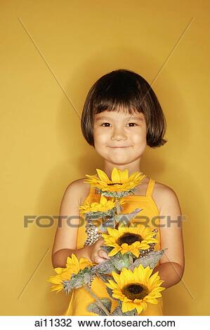 Young girl standing against yellow background, holding flowers, smiling View Large Photo Image Stock Image - Young girl standing against yellow background, holding flowers, smiling. Fotosearch