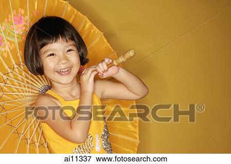 Stock Photo - Young girl standing against yellow background, holding umbrella, laughing. Fotosearch