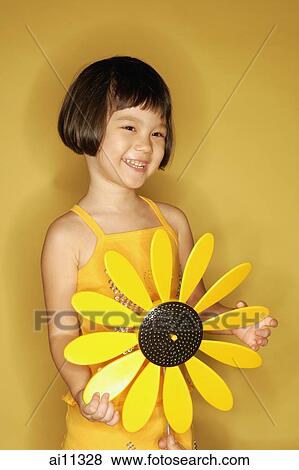 Young girl standing holding plastic sunflower, smiling View Large Photo Image Stock Photo - Young girl standing holding plastic sunflower, smiling. Fotosearch