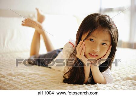 Young girl with hands on chin, lying on bed, looking at camera View Large Photo Image Picture - Young girl with hands on chin, lying on bed, looking at camera. Fotosearch