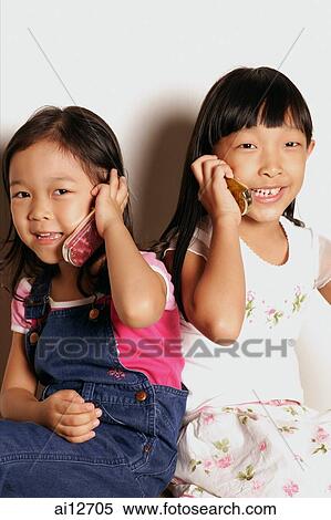 Young girls sitting side by side holding phones View Large Photo Image Stock Photography - Young girls sitting side by side holding phones. Fotosearch