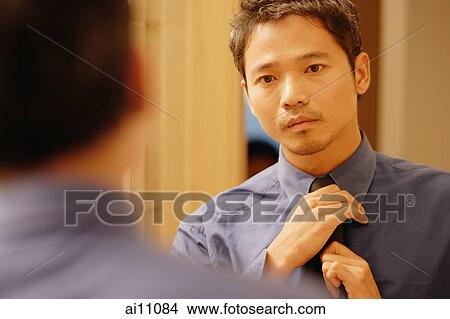 Young man adjusting tie, looking in mirror View Large Photo Image Picture - Young man adjusting tie, looking in mirror. Fotosearch