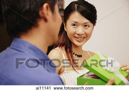 Young man and woman holding gift box, looking at each other View Large Photo Image Stock Image - Young man and woman holding gift box, looking at each other. Fotosearch