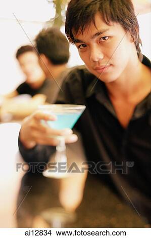 Young man at bar counter holding cocktail glass View Large Photo Image Picture - Young man at bar counter holding cocktail glass. Fotosearch