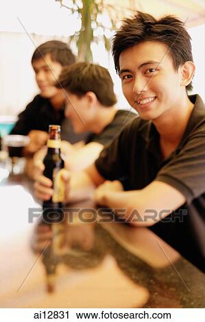 Young man at bar counter with beer bottle, people in the background View Large Photo Image Stock Image - Young man at bar counter with beer bottle, people in the background. Fotosearch