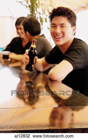 Young man at bar counter with beer bottle, smiling at camera View Large Photo Image Stock Image - Young man at bar counter with beer bottle, smiling at camera. Fotosearch