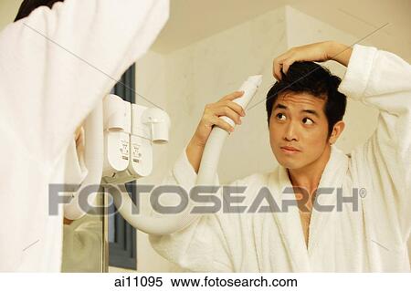 Stock Photography - Young man blow drying hair, looking in mirror. Fotosearch