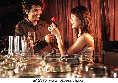Stock Photography - Young man giving young woman a rose at night club. Fotosearch
