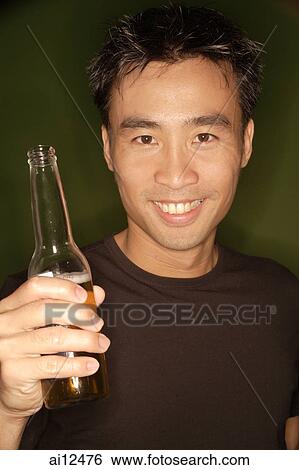 Stock Photograph -  Young man holding beer bottle, portrait. Fotosearch