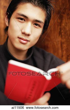 Young man holding book, looking at camera View Large Photo Image Stock Photograph - Young man holding book, looking at camera. Fotosearch