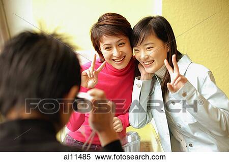 Stock Photography - Young man holding camera, two women posing for picture, making peace sign. Fotosearch