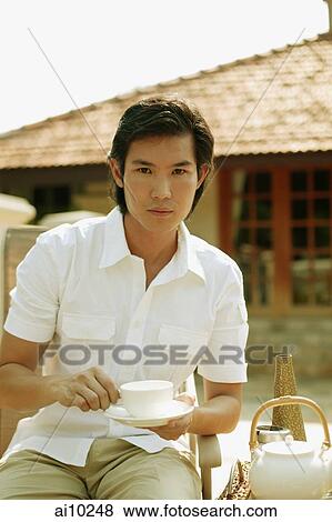 Stock Photo - Young man holding cup and saucer, looking at camera. Fotosearch