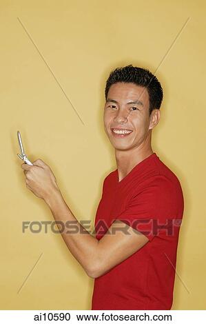 Young man holding mobile phone, looking at camera View Large Photo Image Stock Image - Young man holding mobile phone, looking at camera. Fotosearch