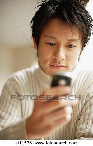 Young man holding mobile phone, looking down View Large Photo Image Stock Photograph - Young man holding mobile phone, looking down. Fotosearch