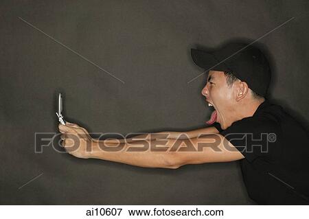 Young man holding mobile phone, making a face View Large Photo Image Stock Photo - Young man holding mobile phone, making a face. Fotosearch