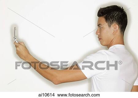 Young man holding mobile phone, side view View Large Photo Image Picture - Young man holding mobile phone, side view. Fotosearch