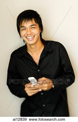Young man holding mobile phone, smiling at camera, portrait View Large Photo Image Stock Photo - Young man holding mobile phone, smiling at camera, portrait. Fotosearch
