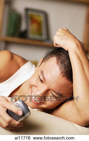 Young man holding mobile phone, smiling View Large Photo Image Stock Photograph - Young man holding mobile phone, smiling. Fotosearch