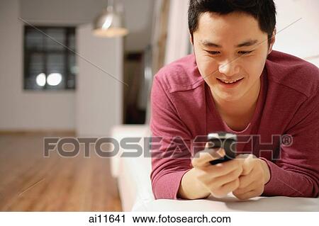 Stock Image - Young man holding mobile phone, text messaging. Fotosearch