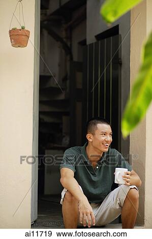 Young man holding mug, sitting at doorway View Large Photo Image Stock Photo - Young man holding mug, sitting at doorway. Fotosearch