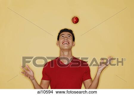 Picture - Young man juggling a ball, yellow background. Fotosearch
