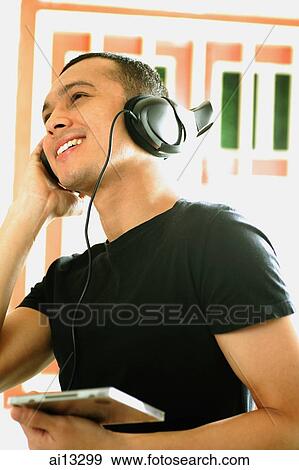 Young man listening to music, wearing headphones, looking away View Large Photo Image Stock Photo - Young man listening to music, wearing headphones, looking away. Fotosearch