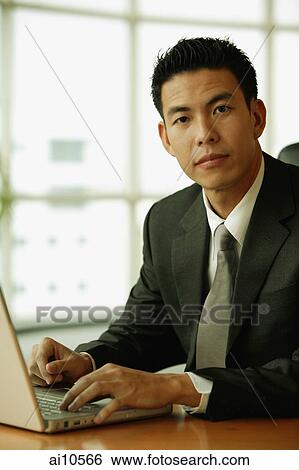 Young man looking at camera, laptop open in front of him View Large Photo Image Stock Photograph - Young man looking at camera, laptop open in front of him. Fotosearch