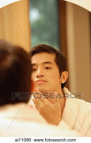 Young man looking in mirror, touching his face View Large Photo Image Stock Image - Young man looking in mirror, touching his face. Fotosearch