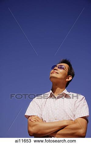 Stock Image - Young man looking up, arms folded. Fotosearch