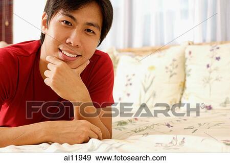 Young man lying on bed, hand on chin, looking at camera View Large Photo Image Stock Photo - Young man lying on bed, hand on chin, looking at camera. Fotosearch