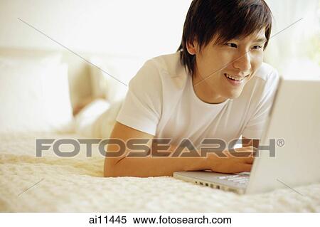 Young man lying on bed, reading from laptop View Large Photo Image Stock Photography - Young man lying on bed, reading from laptop. Fotosearch