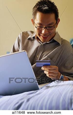 Young man on bed using laptop, holding credit card View Large Photo Image Stock Photo - Young man on bed using laptop, holding credit card. Fotosearch