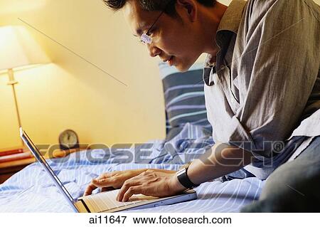 Young man on bed using laptop View Large Photo Image Stock Photo - Young man on bed using laptop. Fotosearch