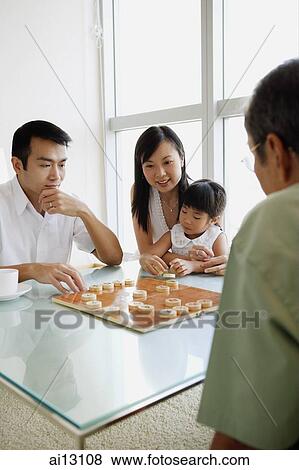 Young man playing Chinese chess with older man, woman and child watching View Large Photo Image Stock Photo - Young man playing Chinese chess with older man, woman and child watching. Fotosearch