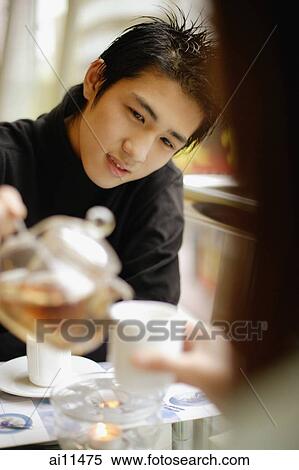 Stock Photography - Young man pouring tea for young woman in front of him.. Fotosearch