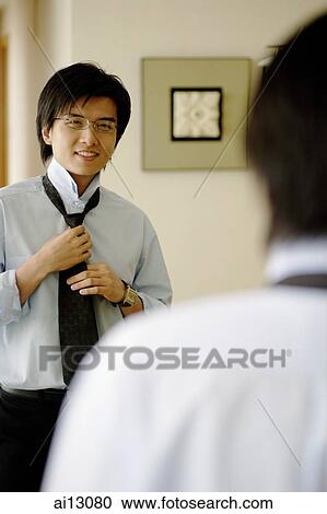Young man putting on tie, looking at mirror View Large Photo Image Stock Image - Young man putting on tie, looking at mirror. Fotosearch