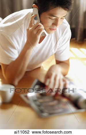 Young man reading magazine while on the phone View Large Photo Image Stock Image - Young man reading magazine while on the phone. Fotosearch