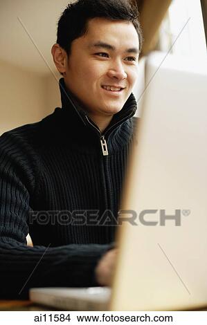 Young man sitting at table using laptop View Large Photo Image Picture - Young man sitting at table using laptop. Fotosearch