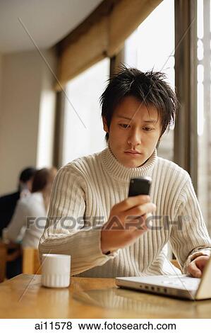 Young man sitting at table with laptop and mobile phone View Large Photo Image Stock Photo - Young man sitting at table with laptop and mobile phone. Fotosearch