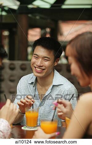 Young man sitting with friends, having a drink View Large Photo Image Picture - Young man sitting with friends, having a drink. Fotosearch